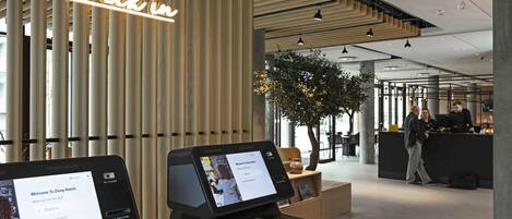 A modern hotel reception area with a 'Check-in' sign, a digital kiosk, and a reception desk.
