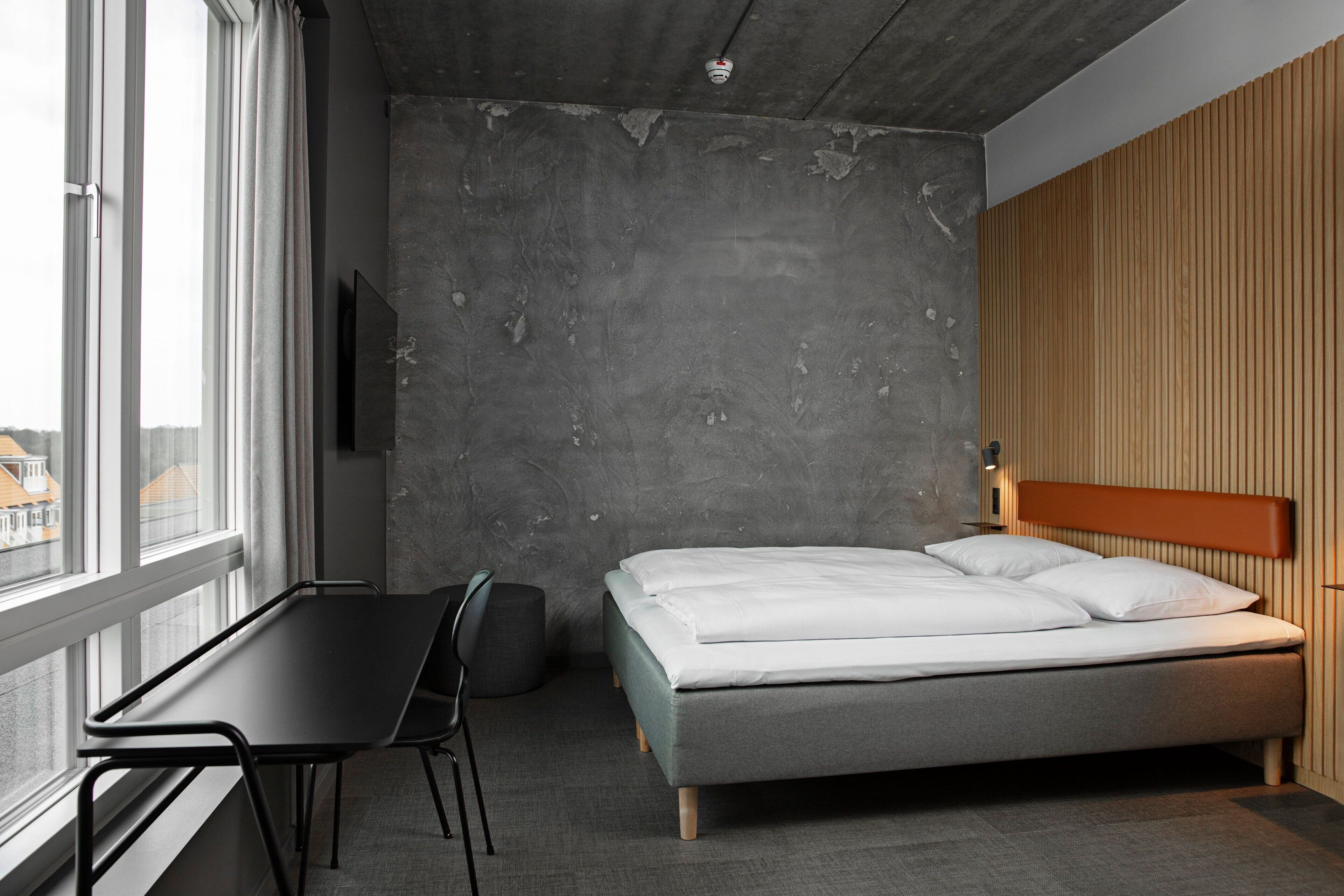 A modern hotel room with a bed, a desk, and a chair.