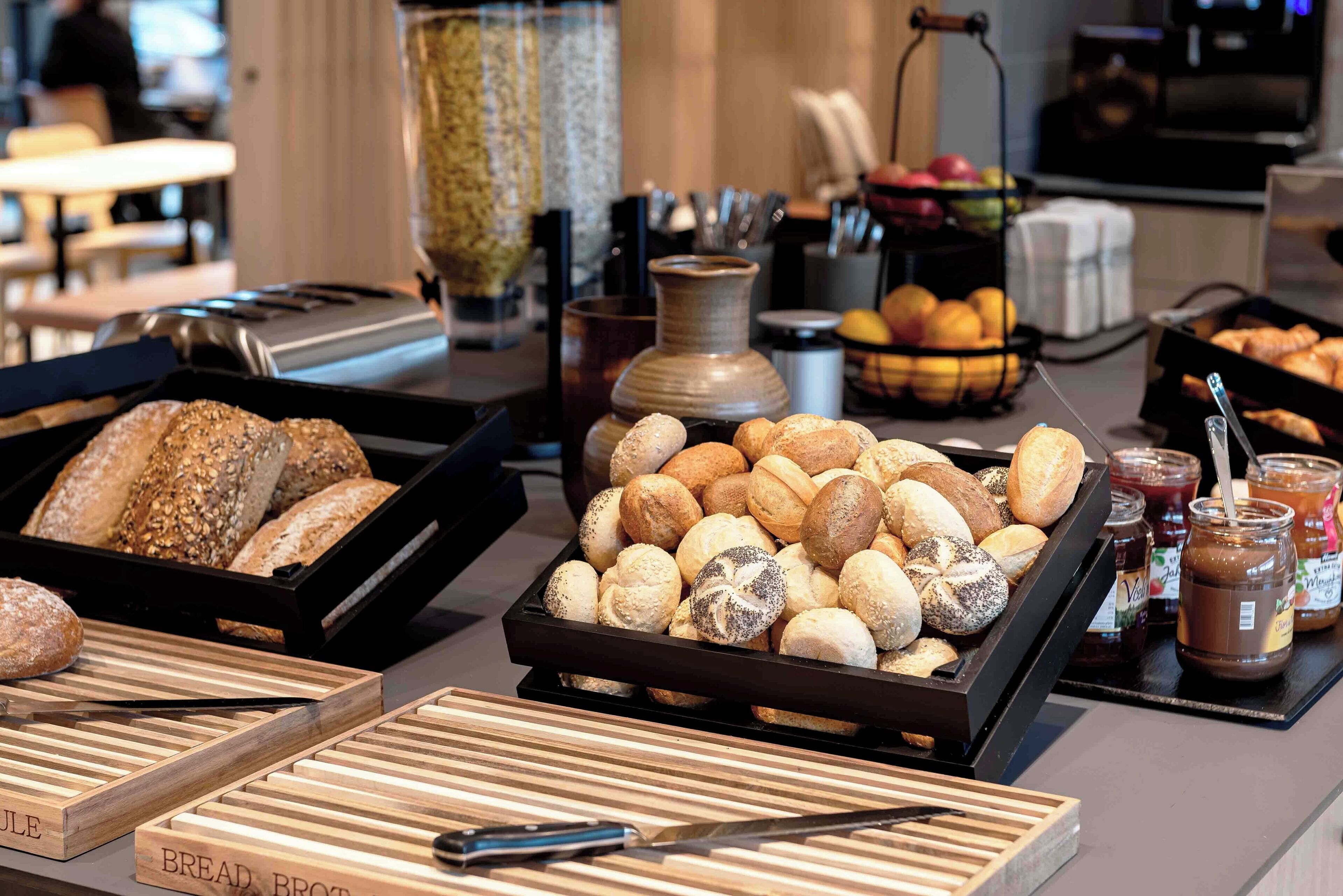 A buffet with various breads and pastries, a coffee machine, and a fruit bowl.