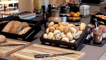 Ein reichhaltiges Buffet mit verschiedenen Brotsorten und Gebäck, einer Kaffeemaschine sowie einer Obstschale.
