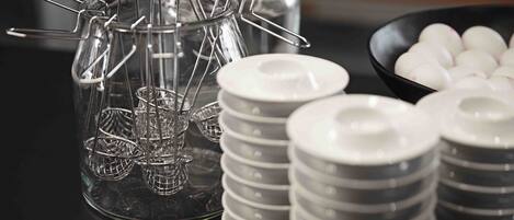A glass jar with metal wire baskets, stacked gray and white plates, and a bowl of white spherical objects.