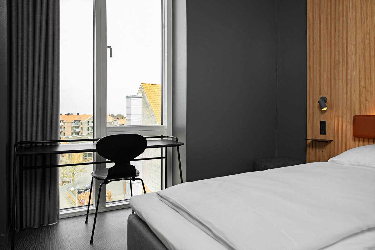 A hotel room with a bed, a desk, and a chair near a window.