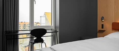 Habitación de hotel con cama, escritorio y silla cerca de una ventana.