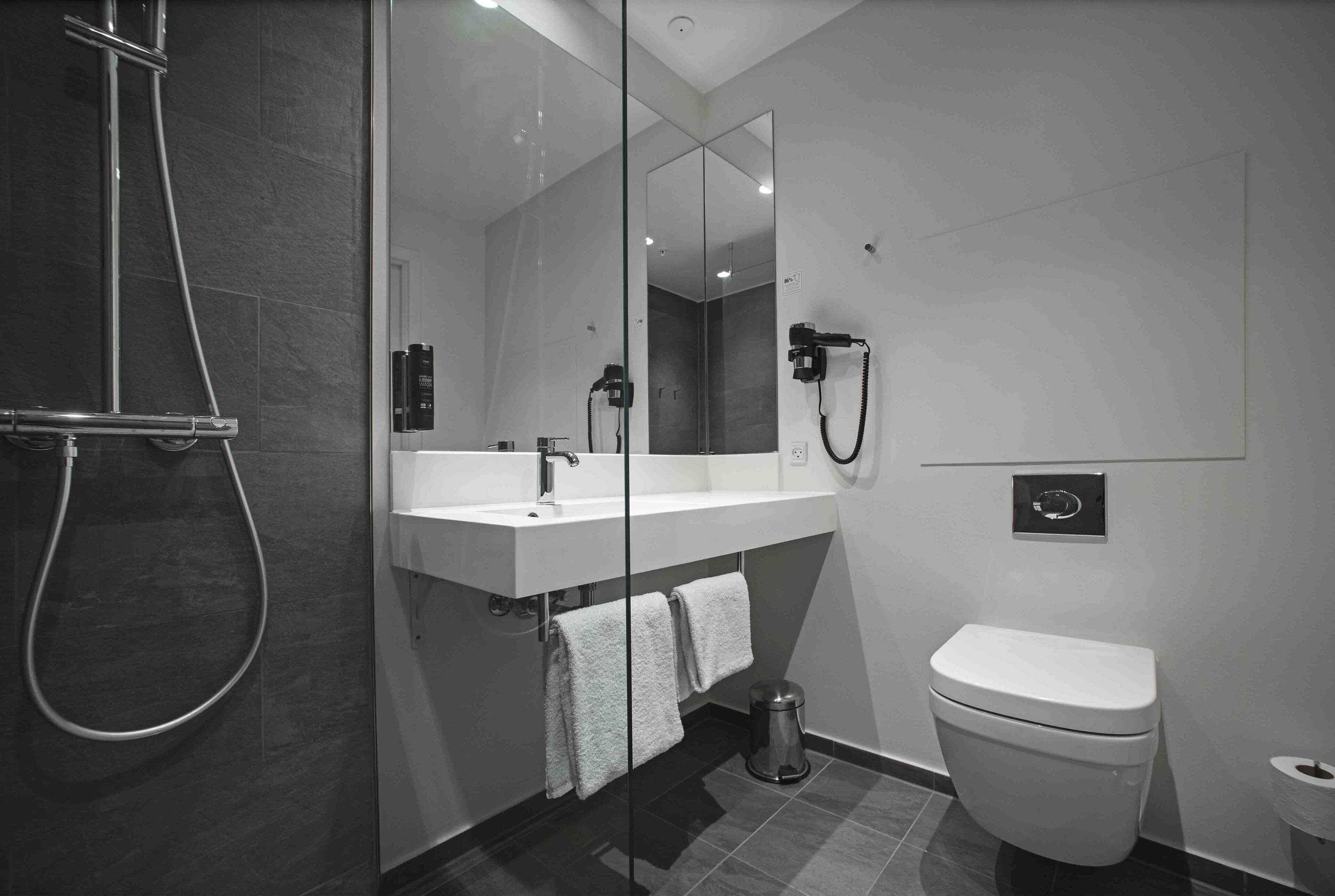 A modern bathroom with a glass-enclosed shower, a white sink with a mirror, and a toilet.