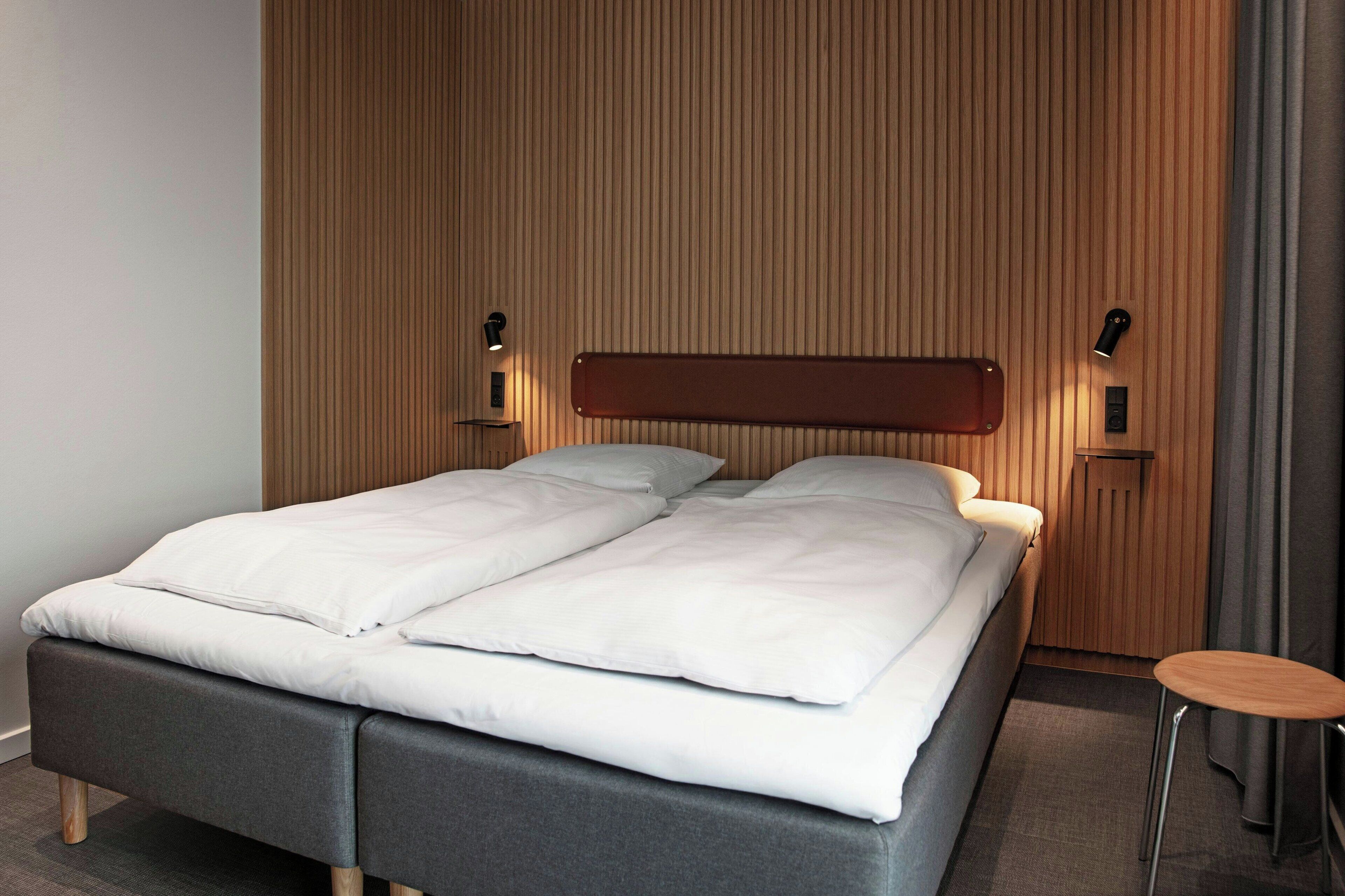 A modern hotel room with a bed, a small table, and a wooden headboard.