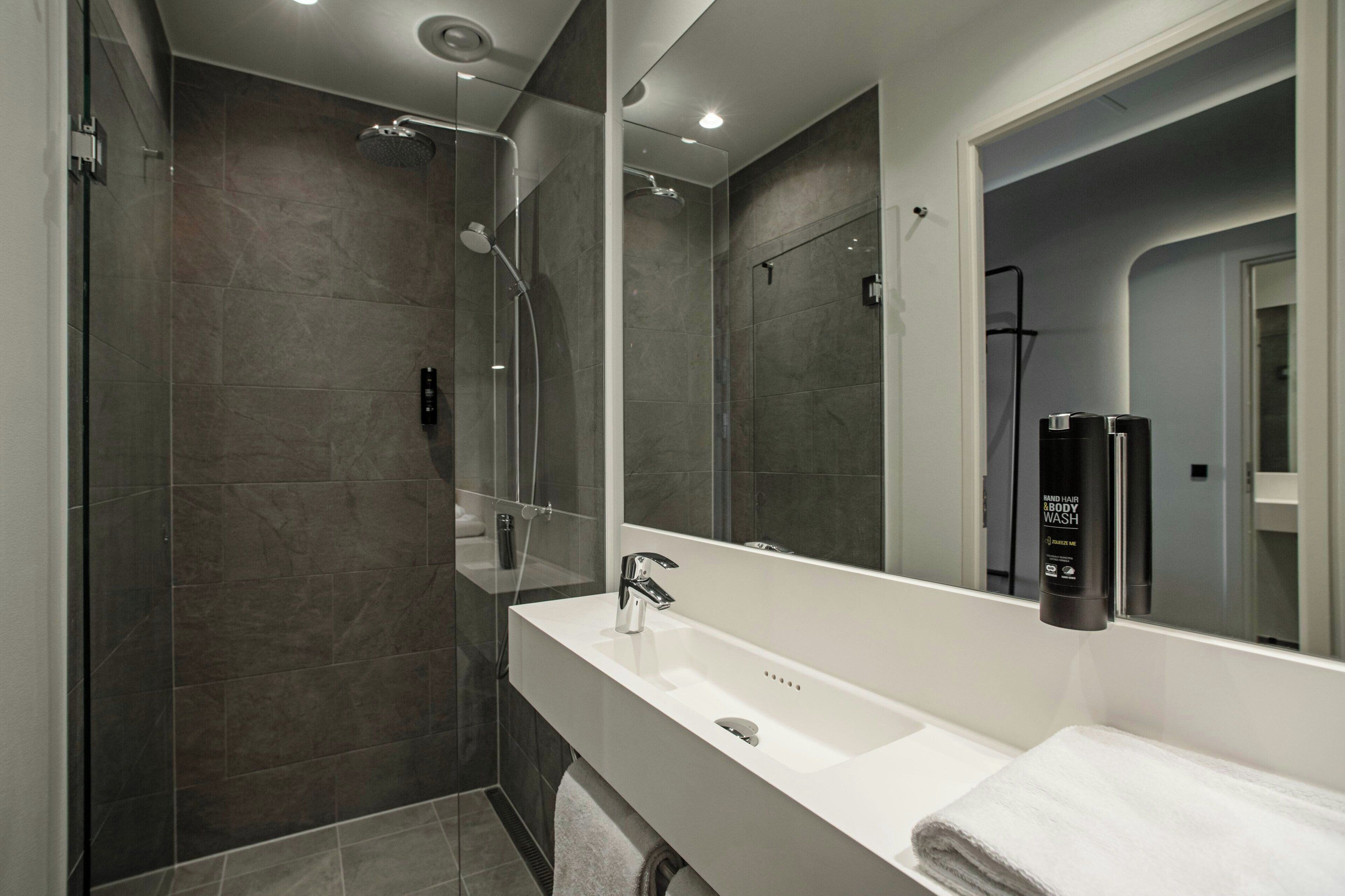 A modern bathroom with a glass-enclosed shower, a white sink, and a large mirror.