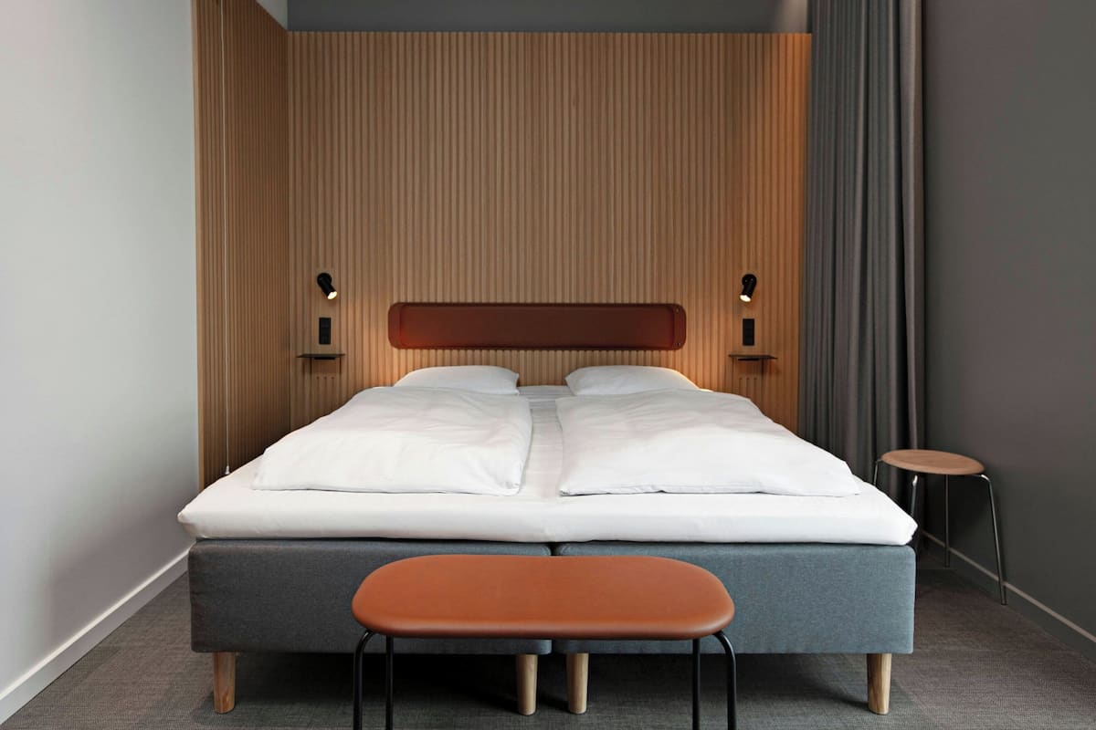 Quarto de hotel moderno com uma cama, um banquinho pequeno e painel de parede de madeira.
