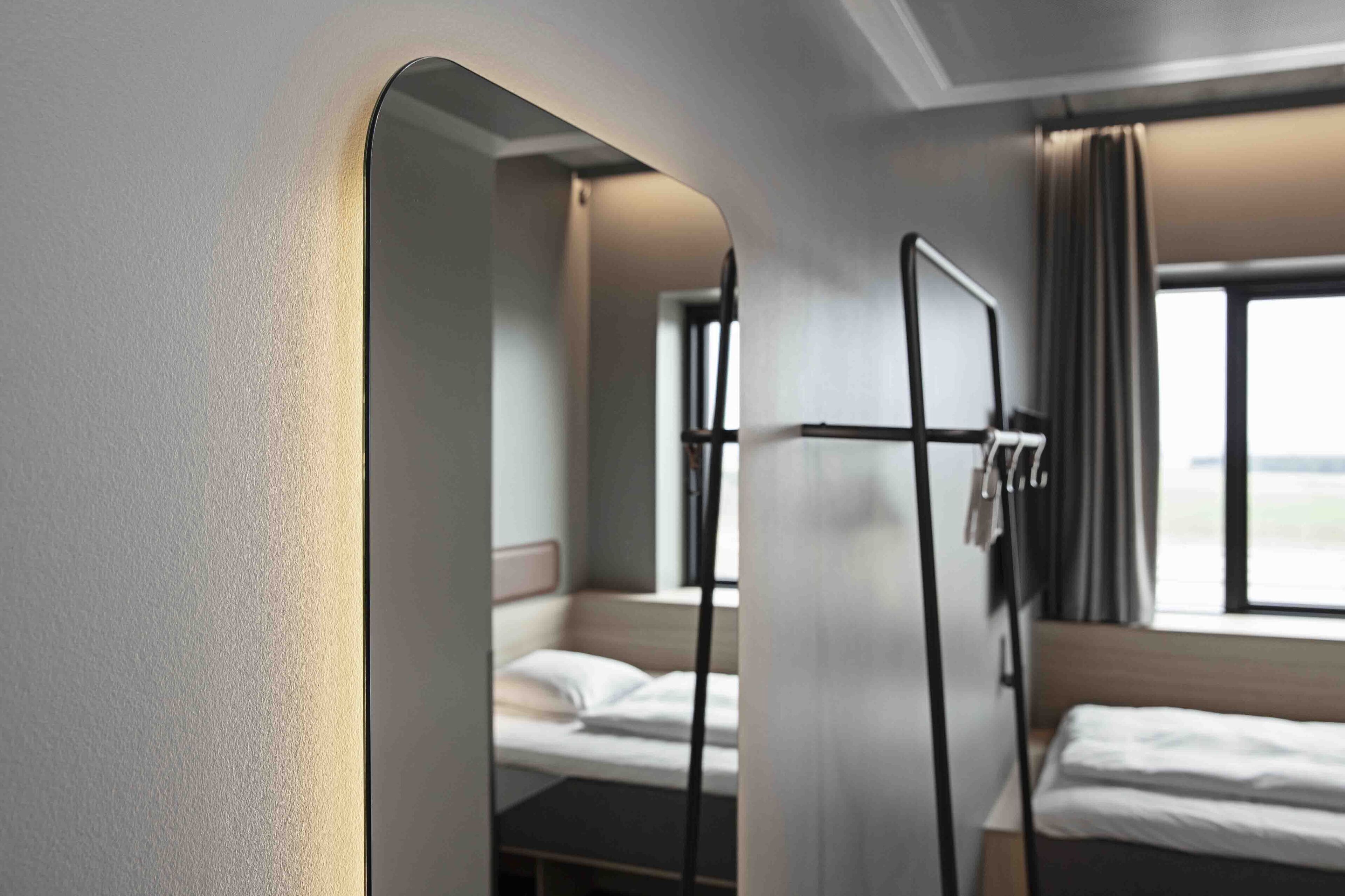 A modern hotel room with a bunk bed, a large mirror, and a window with curtains.
