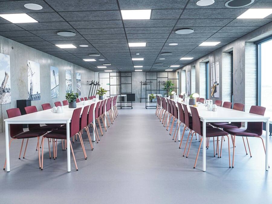 Een vergaderruimte met een lange tafel, rode stoelen en een witte tafelkleed.