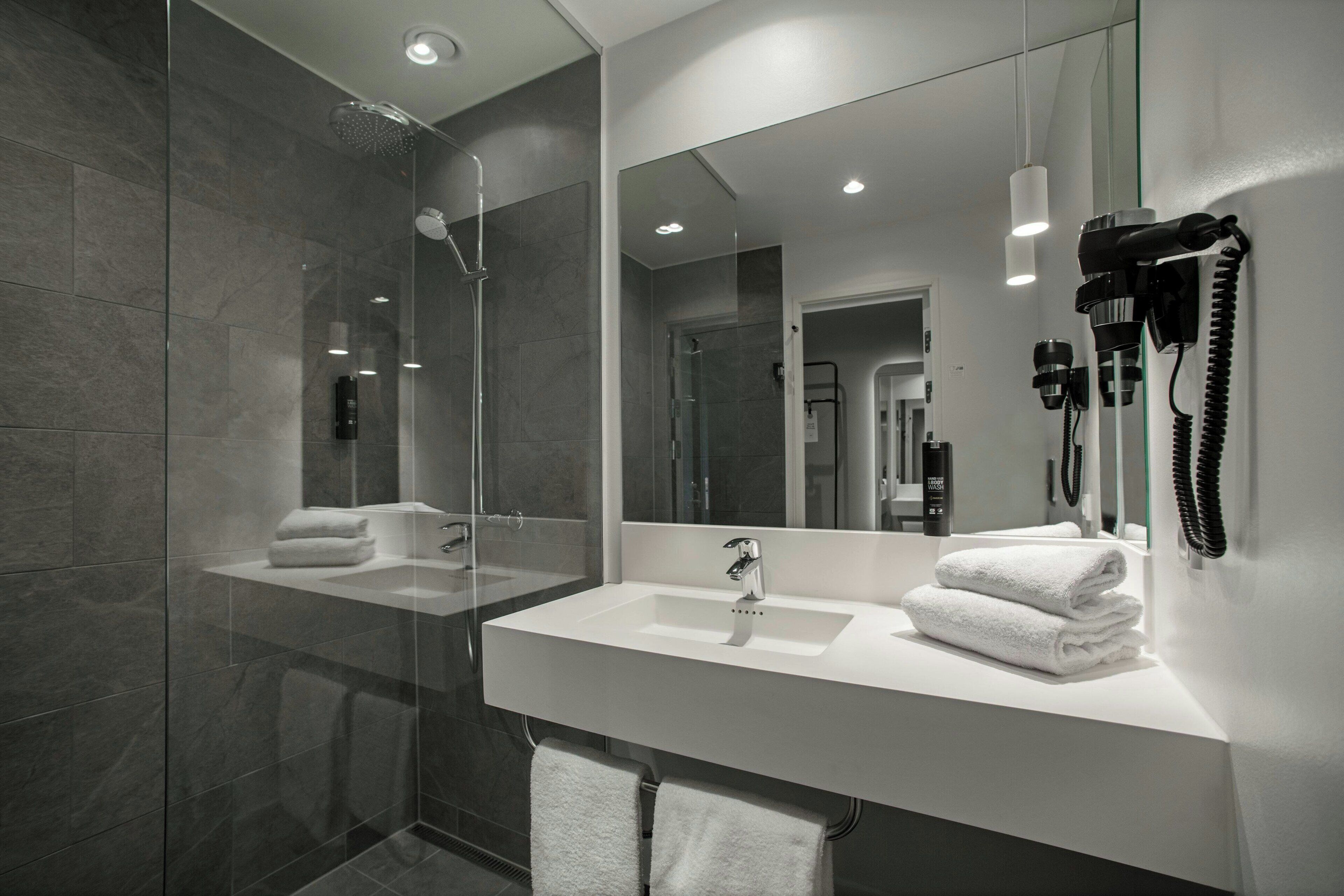 A modern bathroom with a glass shower enclosure, a white sink, and a large mirror.