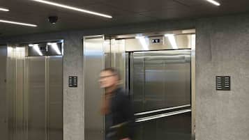 L’intérieur d’un ascenseur, avec des portes métalliques, un écran numérique et un sol recouvert de moquette.