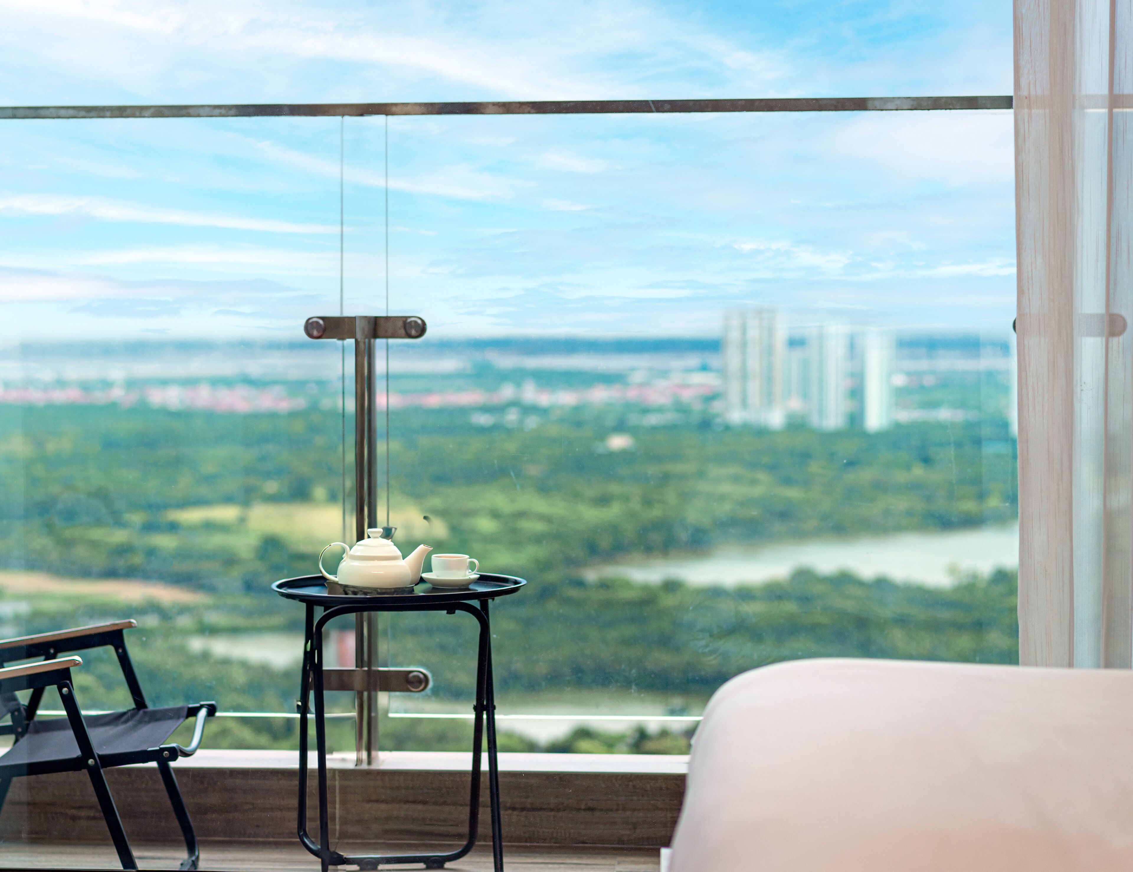 Un balcone con un tavolo su cui si trovano un teiera e una tazza, con vista su un paesaggio urbano ricco di verde e palazzi.