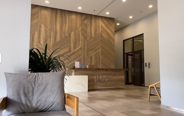 Un área de recepción con pared de madera, mostrador de recepción, una planta y zona de estar.
