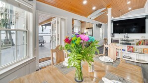 Un comedor con una mesa de madera, sillas, un jarrón de flores y un televisor al fondo.