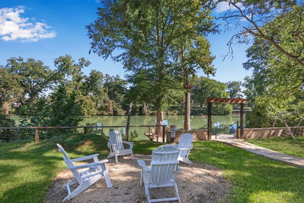 A gazebo with Adirondack chairs in a park with a lake.