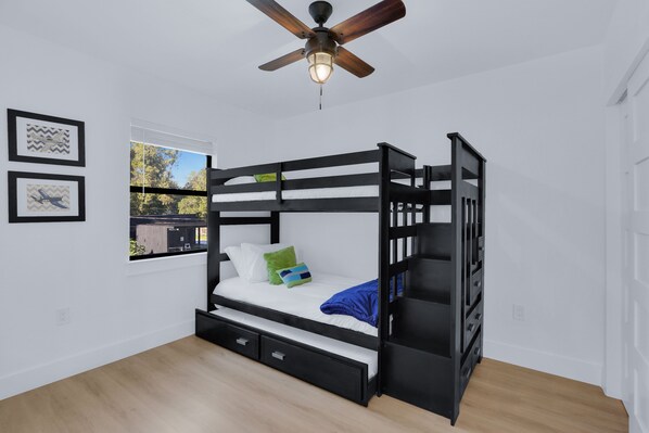 Habitación con literas, ventilador de techo, ventana con vistas y cuadros en la pared.
