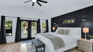 Een moderne slaapkamer met een groot bed, een plafondventilator, een nachtkastje met een lamp en uitzicht door de glazen deuren.