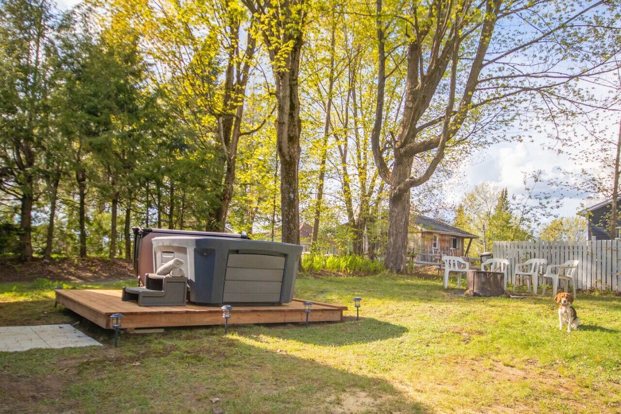 Un bain à remous installé sur une plateforme en bois, dans un jardin avec des arbres et une clôture en bois.