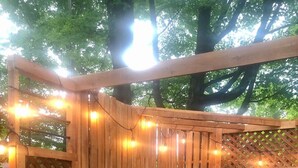 A wooden deck with a hot tub, string lights, and a wooden fence.