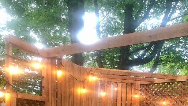 Une terrasse en bois avec un jacuzzi, des guirlandes lumineuses et une clôture en bois.