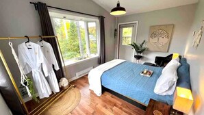 A bedroom with a bed, a bedside table, a hanging robe rack, and a window with curtains.