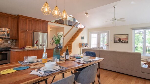 A modern kitchen with wooden cabinets, a dining table set for four, and a staircase leading to an upper level.