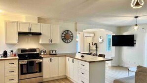 A modern kitchen with white cabinetry, a built-in oven, and a large island. - Chalet BIA - Au courant des 2 rivières (Weedon)