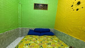 A small, brightly colored room with a bed, pillows, and a plaque on the wall. - OYO Life 93401 Kos Putri Alamanda Syariah (Janapria)