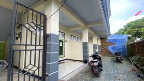 A covered outdoor area with tiled flooring, a metal gate, and two motorcycles parked. - OYO Life 93401 Kos Putri Alamanda Syariah (Janapria)