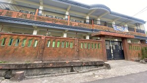 A multi-story building with a balcony on the second floor, a gated entrance, and a sign indicating a school. - OYO Life 93401 Kos Putri Alamanda Syariah (Janapria)
