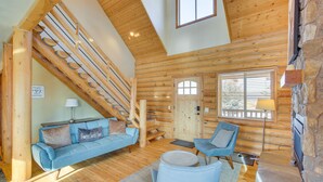 Interno di una baita di legno con una scala in legno, un divano blu, una poltrona e un camino in pietra.