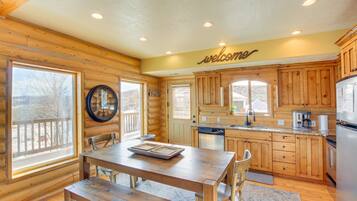 A log cabin kitchen with wooden cabinets, a wooden dining table, and a "welcome" sign.