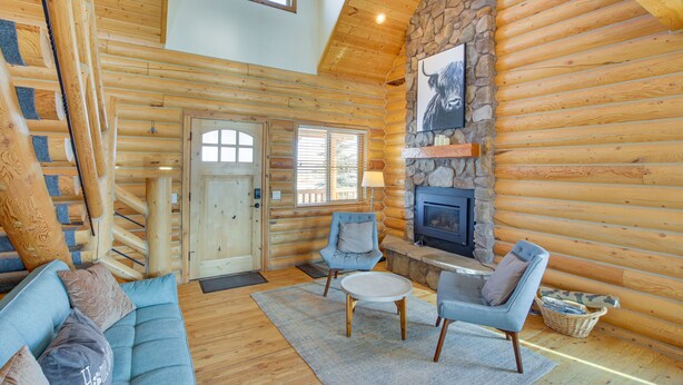 Interno di una baita di legno con camino in pietra, pareti in legno, un divano blu e un tavolo da pranzo.