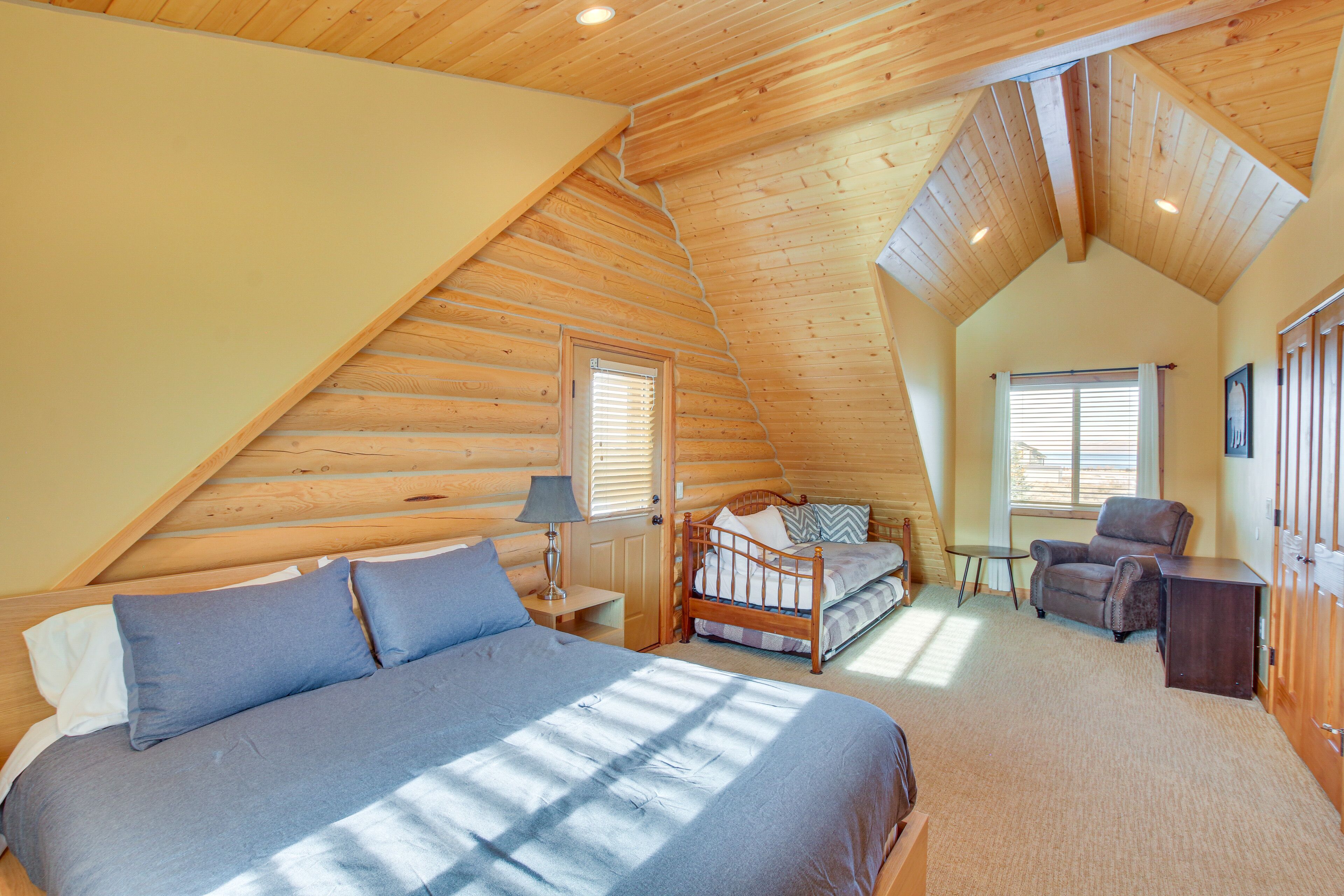 A bedroom with a large bed, a chair, a desk, and a window.