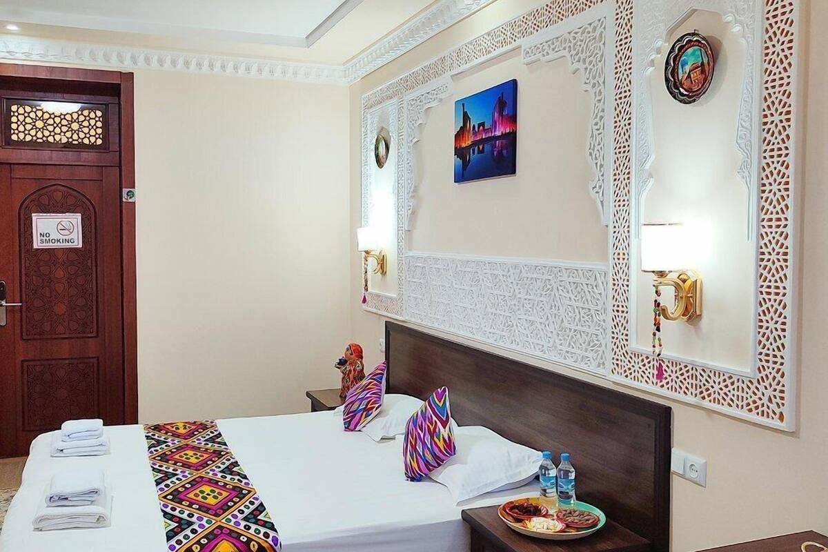Ein Hotelzimmer mit Bett, Nachttisch, Schreibtisch, einer Wand mit Dekoration und einer Tür mit Rauchverbot-Hinweis.