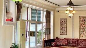 A room with a traditional sofa, decorative hanging lamps, and a large window with shutters. - hotel Shams Bukhara (Bukhara)