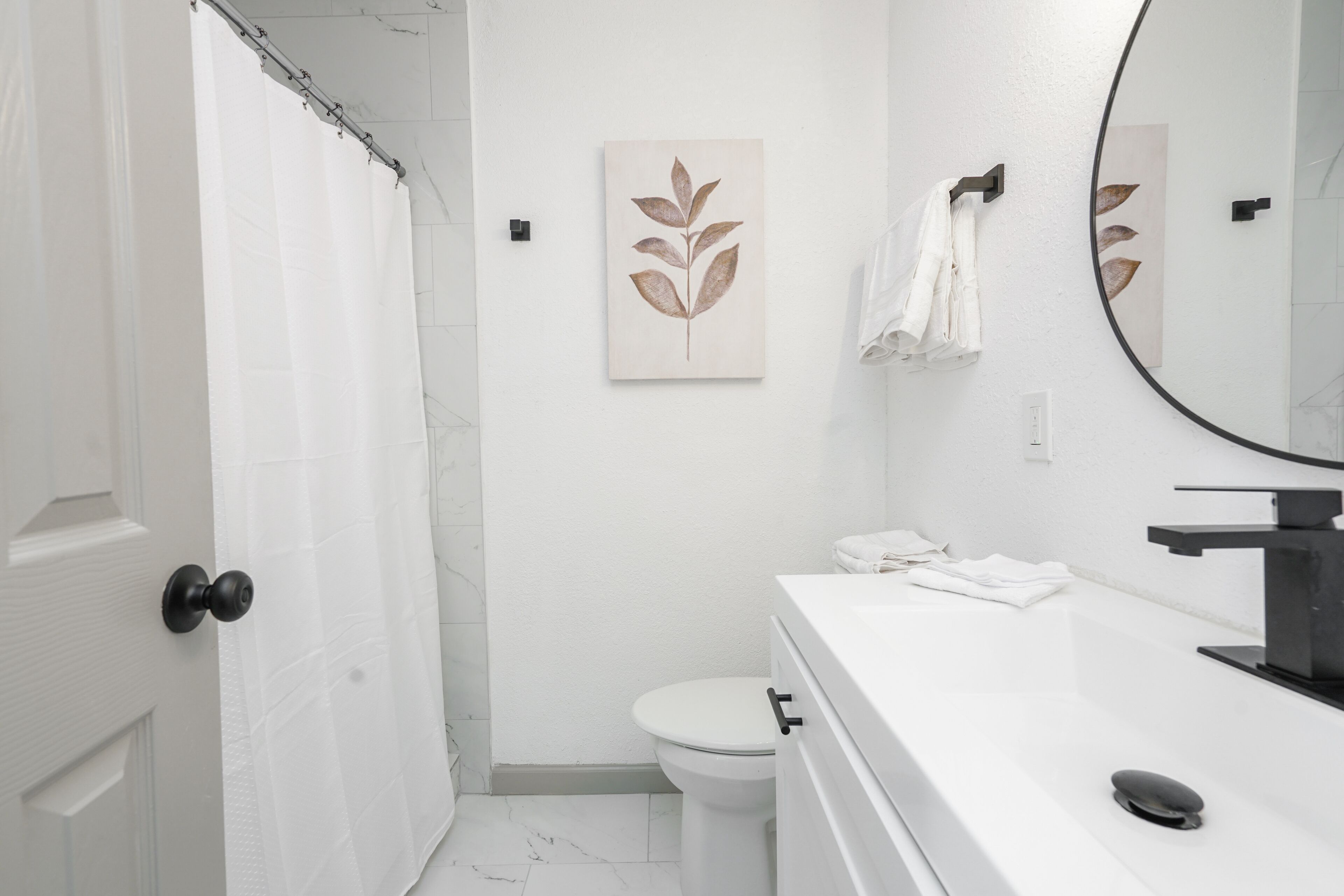 Une salle de bain avec des toilettes blanches, un lavabo blanc avec un robinet noir et un rideau de douche.