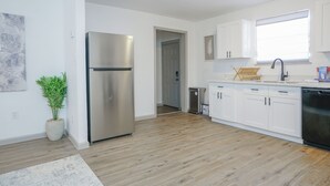 A modern kitchen with white cabinets, a stainless steel refrigerator, and a wooden floor.