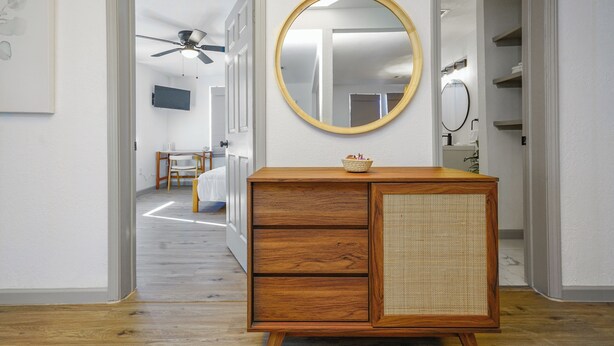 A hallway with a wooden dresser, a round mirror, and a ceiling fan.