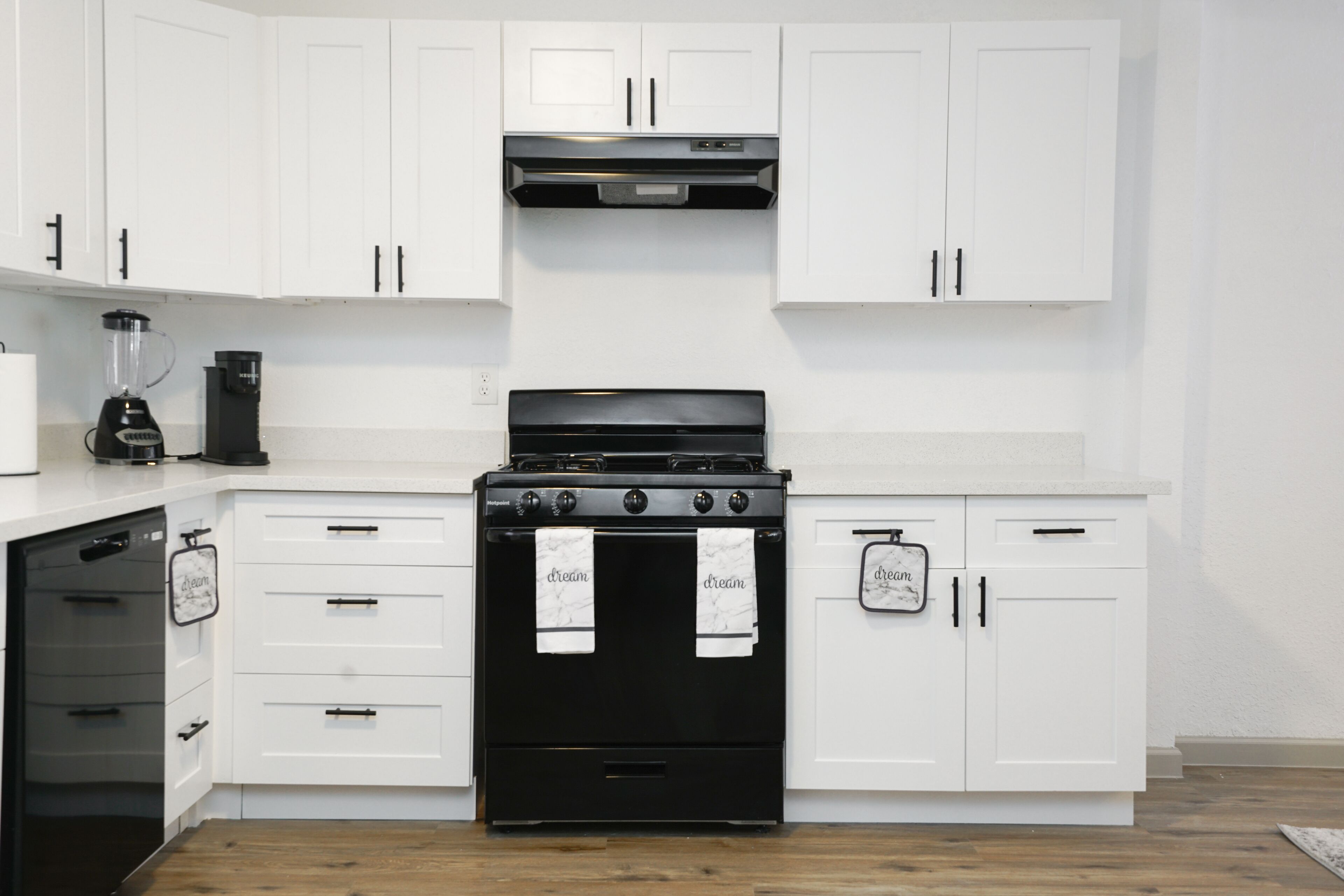 A kitchen with white cabinets, a black stove, and a coffee maker.