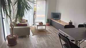 A modern living room with a sofa, a coffee table, a dining table, and a TV. There are potted plants and a large window. - Appartement se Trouvant au Premier Étage D'une Maison Individuelle (Marseille)