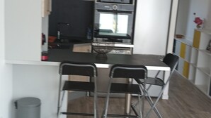 A compact kitchen with modern appliances, a dining area with two chairs, and a hanging light fixture. - Appartement se Trouvant au Premier Étage D'une Maison Individuelle (Marseille)
