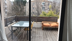 A balcony with a glass table, wooden bench, and orange cushions. - Appartement se Trouvant au Premier Étage D'une Maison Individuelle (Marseille)