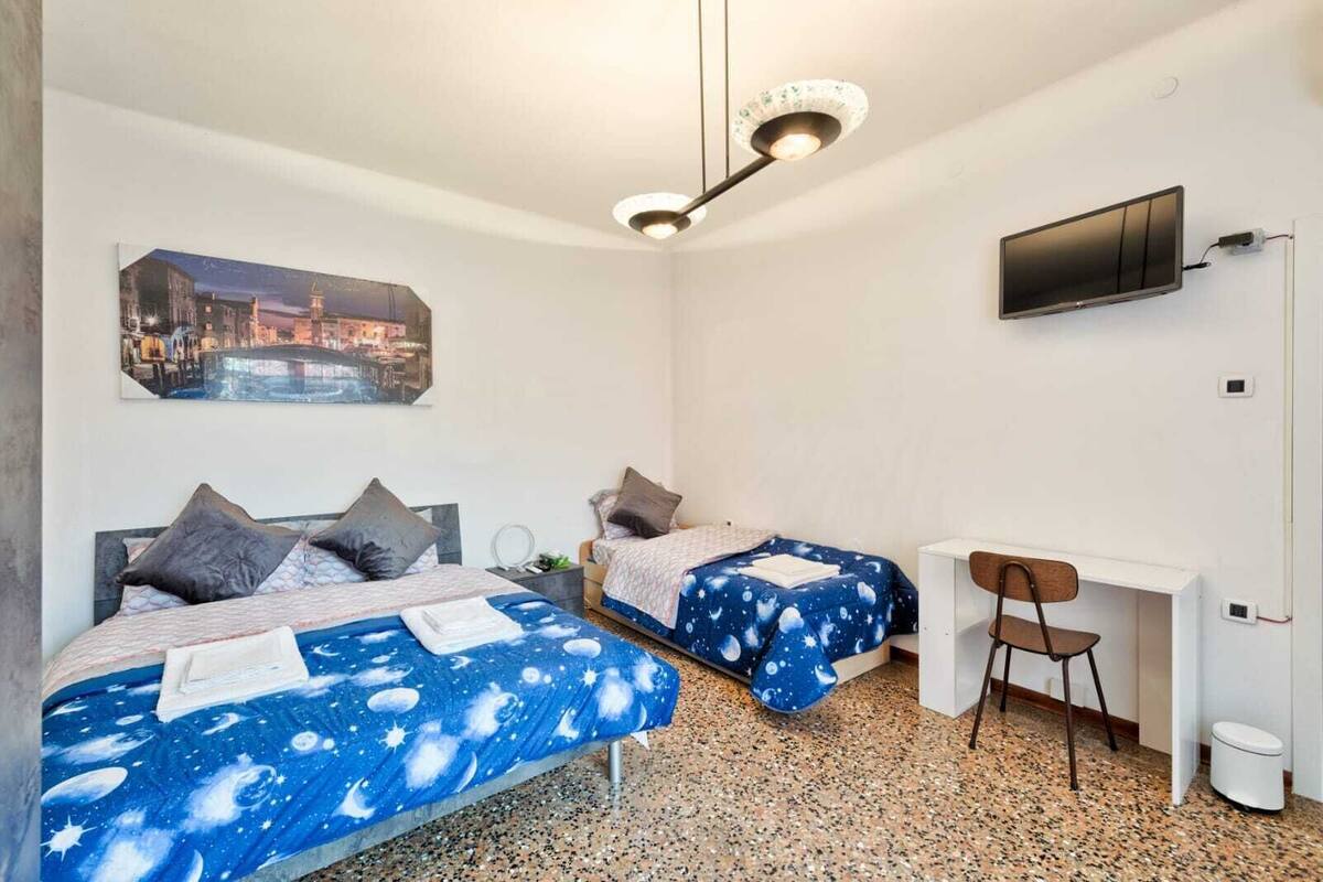 Un dormitorio con dos camas, un escritorio, una silla, un televisor y un cuadro en la pared.