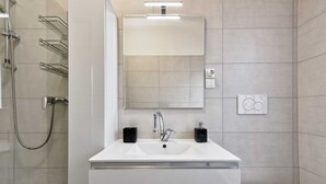 Un baño moderno con un lavamanos blanco, dos dispensadores de jabón negros, un espejo grande y una ducha con cabezal de ducha de mano.