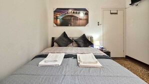 Habitación de hotel con cama, dos almohadas, mesita de noche, lámpara y aire acondicionado instalado en la pared.