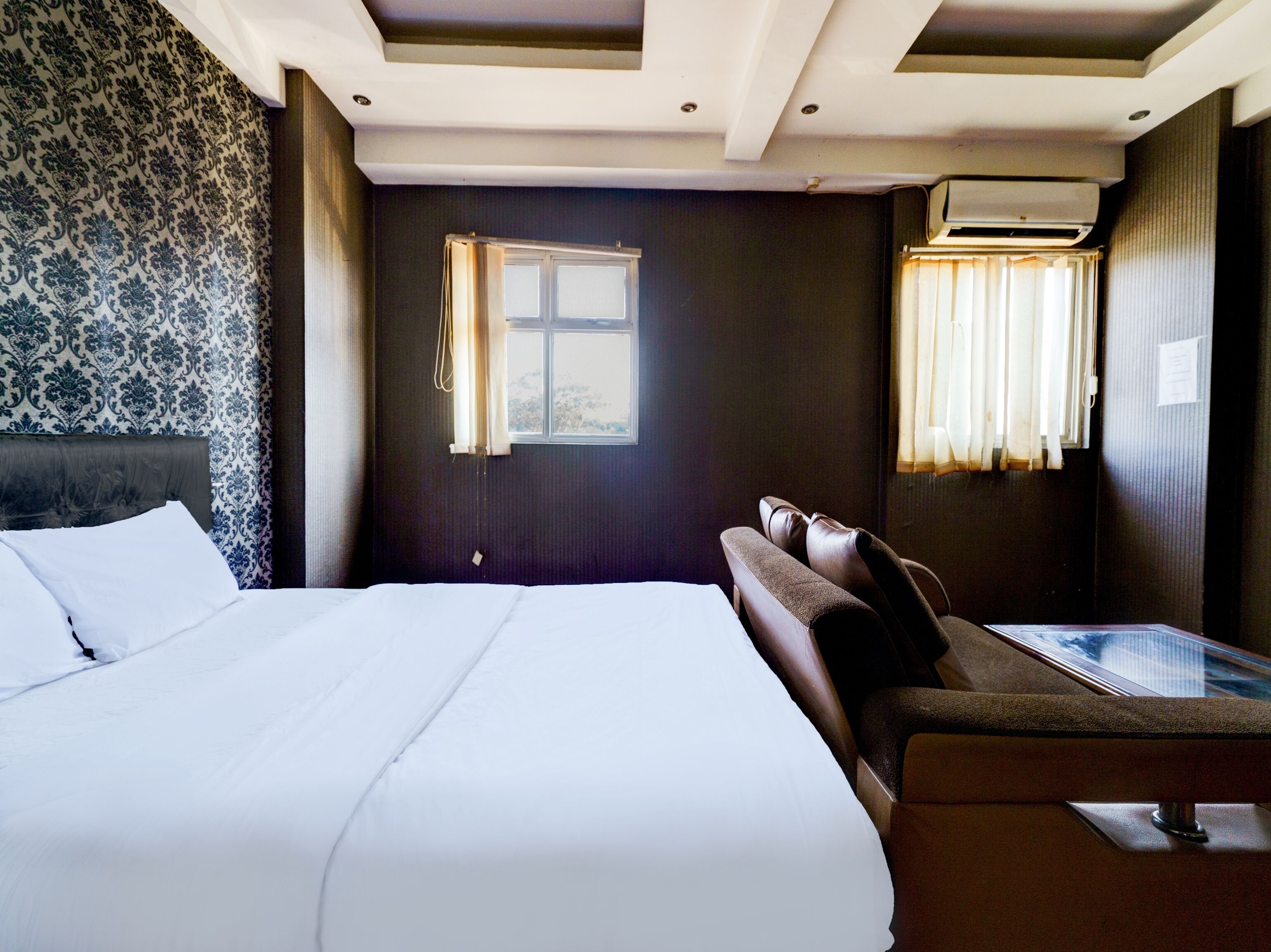 A hotel room with a large bed, a sofa, a small table, and a window with curtains.