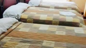 A hotel room with two beds, each with a quilted bedspread.