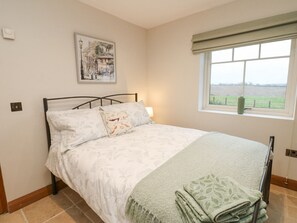 A bedroom with a bed, a window with a view, a painting on the wall, and a bedside lamp. - Sutton Newbold Cottage (Trimdon Station)