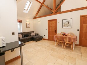 A cozy living room with a brown leather sofa, a dining table with wooden chairs, and a wooden door. - Sutton Newbold Cottage (Trimdon Station)